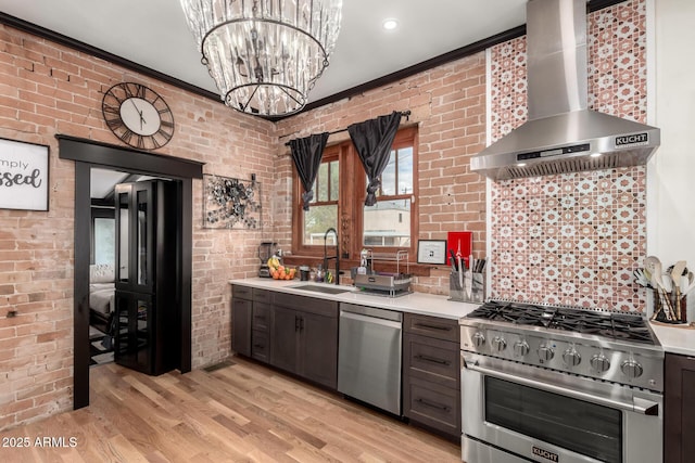 kitchen with a sink, appliances with stainless steel finishes, wall chimney exhaust hood, and brick wall