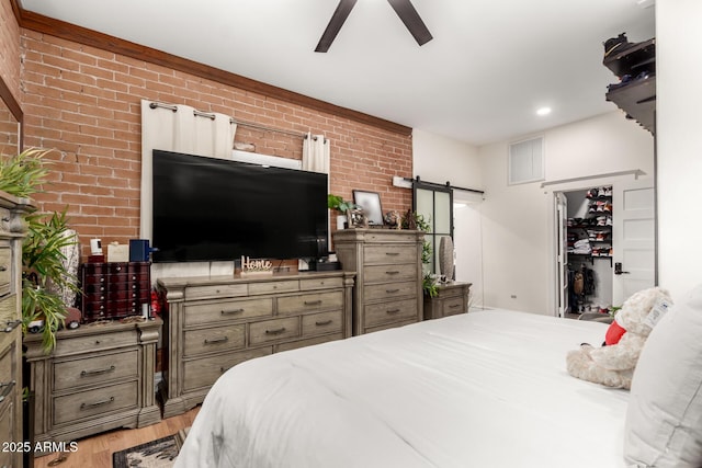 bedroom with light wood finished floors, visible vents, brick wall, and a barn door