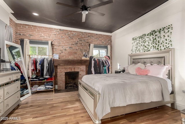 bedroom featuring light wood-style flooring, multiple windows, ornamental molding, and brick wall