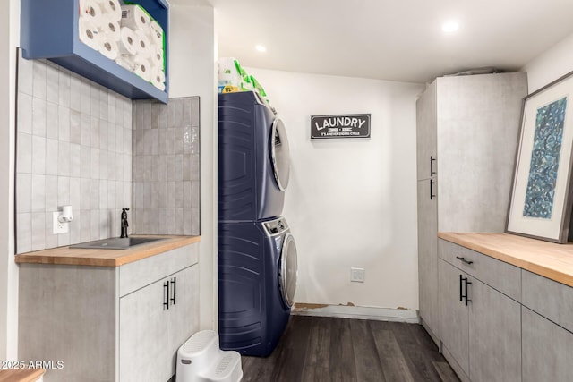 laundry room with dark wood-type flooring, a sink, stacked washing maching and dryer, recessed lighting, and cabinet space