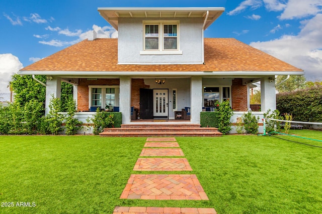 view of front of house with covered porch, a front lawn, and roof with shingles