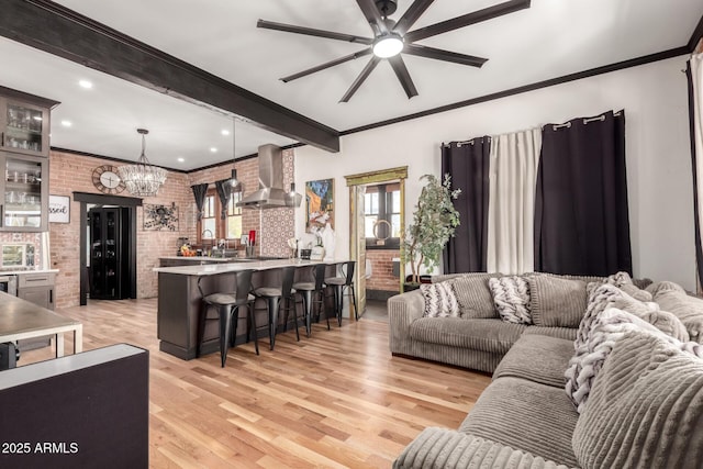 living area featuring brick wall, beamed ceiling, ornamental molding, ceiling fan with notable chandelier, and light wood-style floors