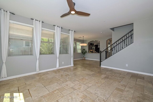 6611 S San Jacinto St, Gilbert, AZ 85298 - unfurnished living room featuring arched walkways, ceiling fan, stone tile flooring, baseboards, and stairway