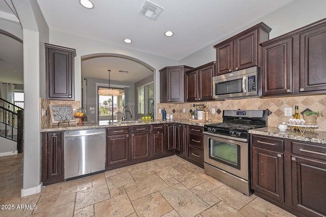 6611 S San Jacinto St, Gilbert, AZ 85298 - kitchen featuring appliances with stainless steel finishes, arched walkways, decorative backsplash, dark brown cabinetry, and light stone countertops