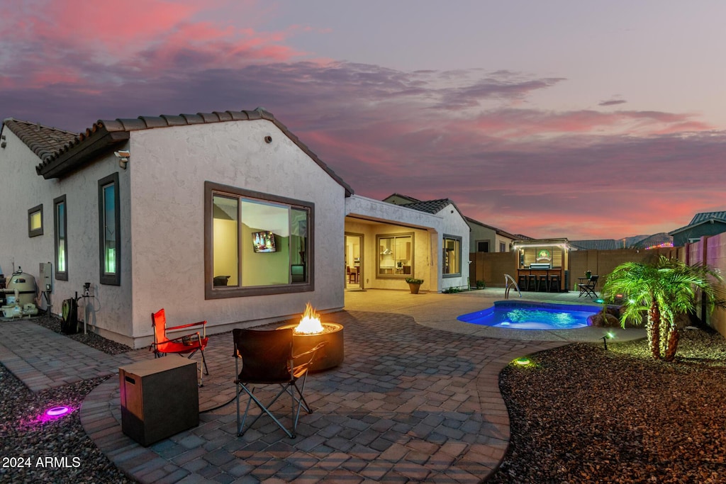 back house at dusk with a fire pit, a fenced in pool, and a patio