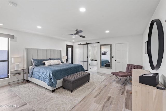 bedroom with a barn door, light hardwood / wood-style floors, ensuite bath, and ceiling fan