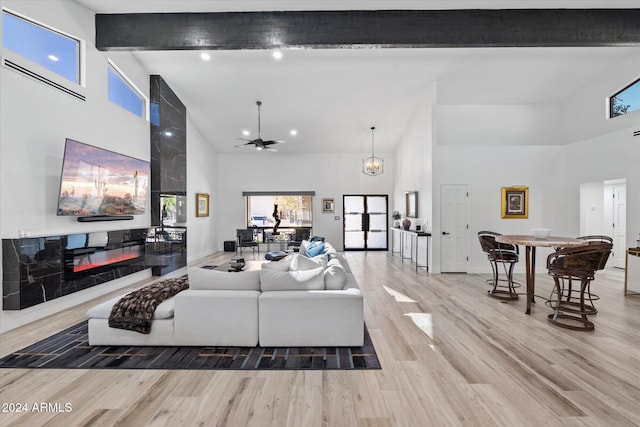 living room with beam ceiling, a large fireplace, light hardwood / wood-style floors, and a high ceiling