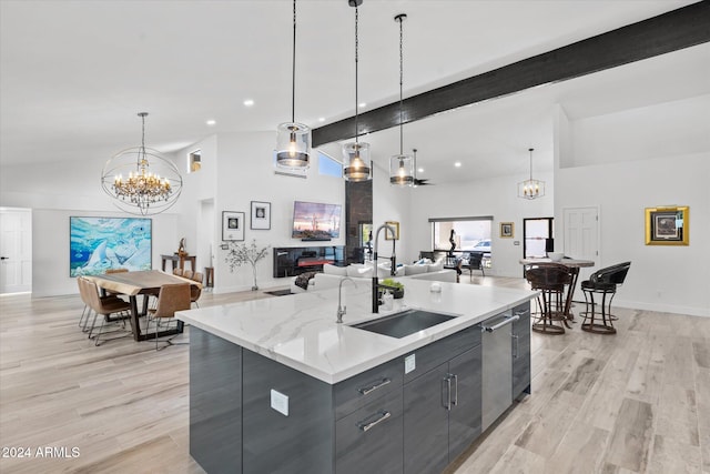 kitchen featuring a large island with sink, sink, hanging light fixtures, and light hardwood / wood-style flooring