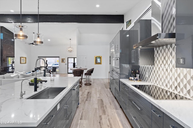 kitchen featuring light stone counters, black electric cooktop, sink, wall chimney range hood, and decorative light fixtures