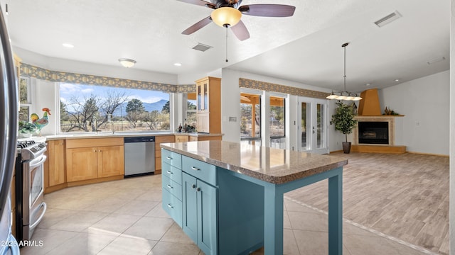 kitchen featuring appliances with stainless steel finishes, ceiling fan, light tile patterned floors, decorative light fixtures, and a fireplace