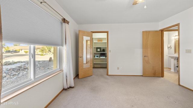 bedroom with connected bathroom, ceiling fan, light colored carpet, and a spacious closet