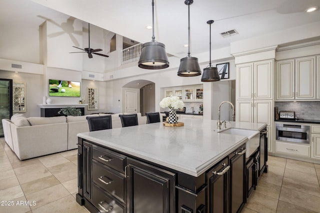 kitchen featuring sink, light stone counters, ceiling fan, an island with sink, and pendant lighting