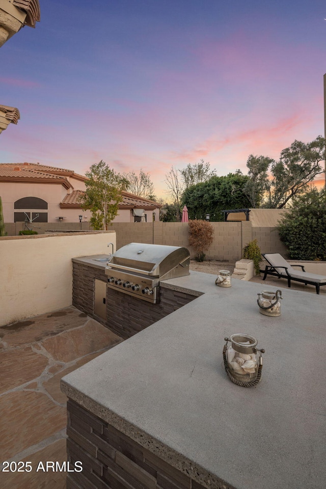 patio terrace at dusk featuring exterior kitchen and grilling area