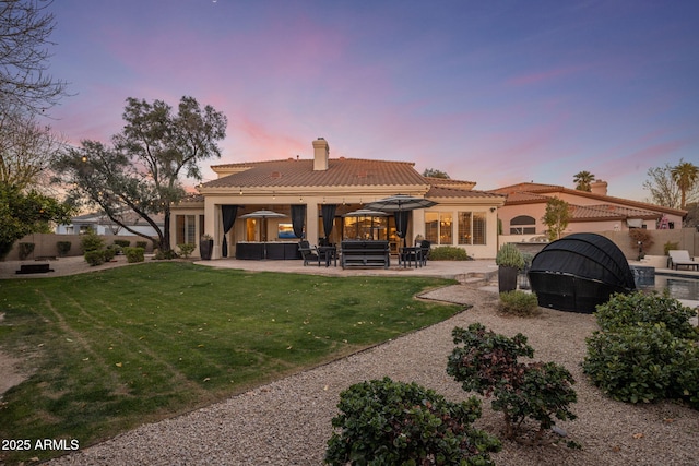 back house at dusk with a patio, a yard, and outdoor lounge area