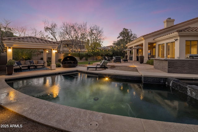 pool at dusk featuring a bar, a patio, an outdoor hangout area, and exterior kitchen