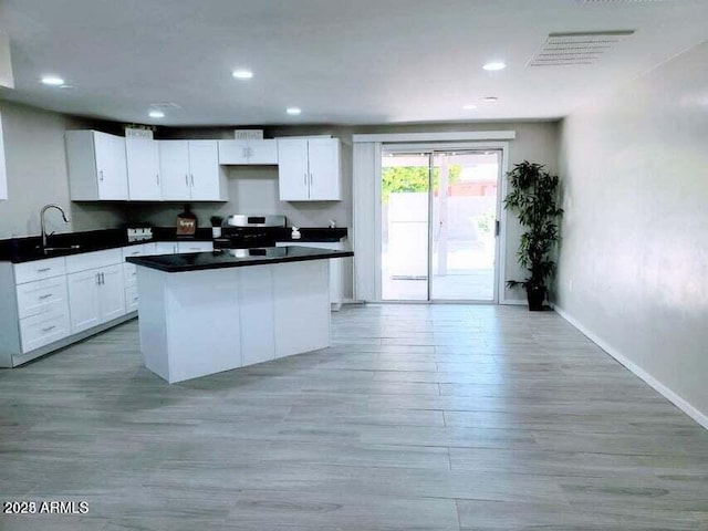 kitchen featuring a kitchen island, sink, white cabinets, stainless steel range oven, and light hardwood / wood-style flooring