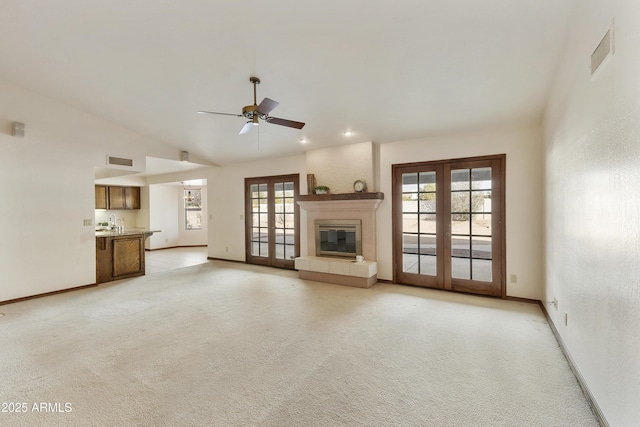 unfurnished living room featuring high vaulted ceiling, a tiled fireplace, ceiling fan, light carpet, and french doors