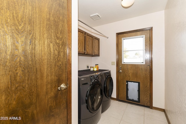 clothes washing area featuring cabinets, light tile patterned floors, and washer and clothes dryer