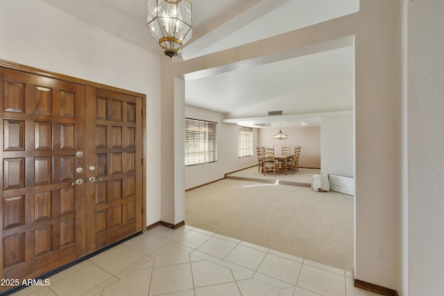 entryway featuring lofted ceiling, light colored carpet, and a chandelier