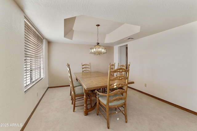 dining room featuring light carpet, a notable chandelier, a textured ceiling, and a tray ceiling