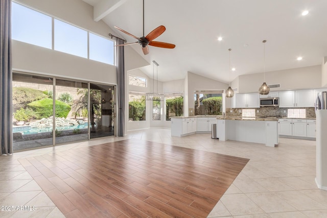 unfurnished living room with high vaulted ceiling, plenty of natural light, and ceiling fan