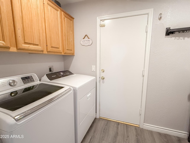 clothes washing area featuring cabinet space, washing machine and clothes dryer, and wood finished floors