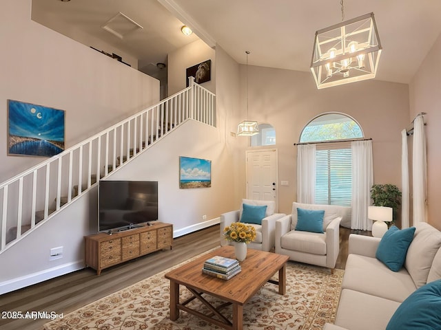 living room with wood finished floors, a towering ceiling, baseboards, stairs, and an inviting chandelier