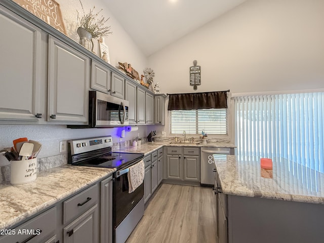 kitchen with light stone counters, gray cabinetry, stainless steel appliances, a sink, and light wood-style floors