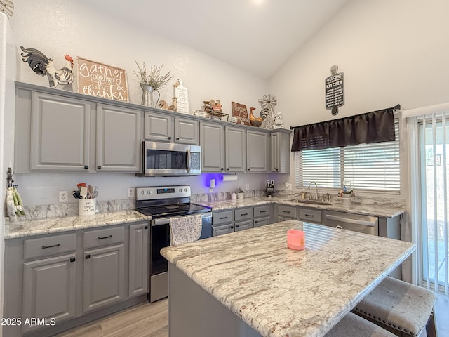 kitchen with a breakfast bar area, a sink, a kitchen island, appliances with stainless steel finishes, and gray cabinets