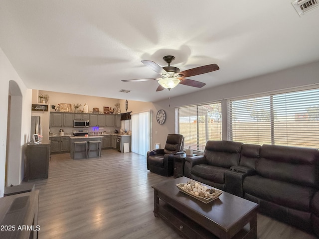 living room featuring arched walkways, wood finished floors, visible vents, and a ceiling fan