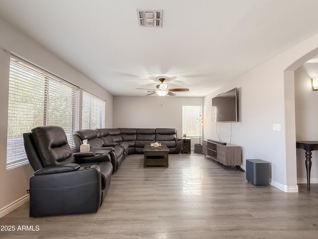 living area with arched walkways, visible vents, light wood-style flooring, ceiling fan, and baseboards