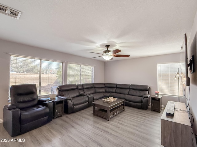 living area featuring light wood-style flooring, a textured ceiling, visible vents, and a ceiling fan