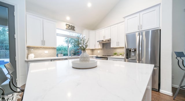 kitchen with appliances with stainless steel finishes, white cabinetry, backsplash, vaulted ceiling, and light stone counters