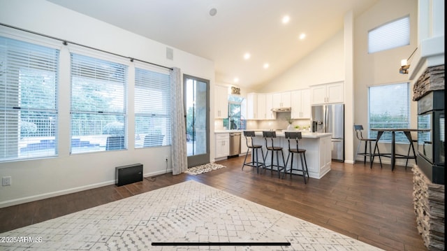 kitchen featuring white cabinets, a center island, stainless steel appliances, high vaulted ceiling, and a breakfast bar area