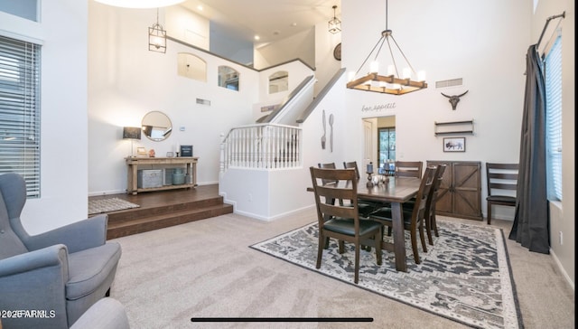 carpeted dining room featuring an inviting chandelier and a high ceiling