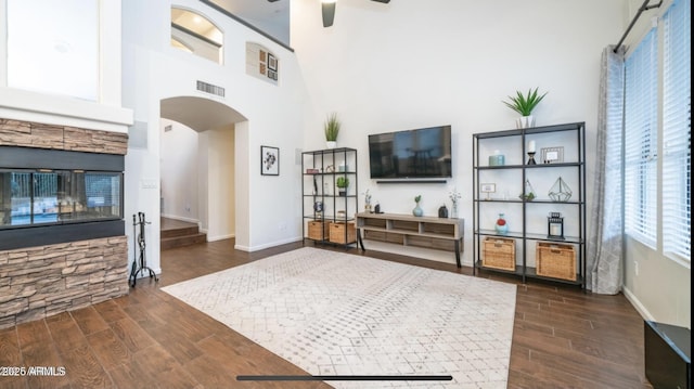 living room featuring ceiling fan, a high ceiling, and a stone fireplace