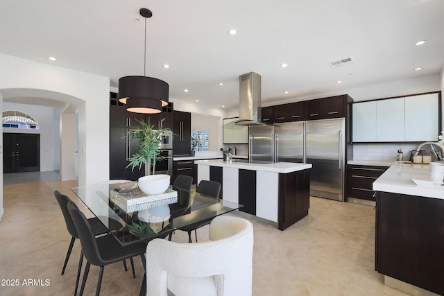 kitchen featuring pendant lighting, tasteful backsplash, an island with sink, island range hood, and high end fridge