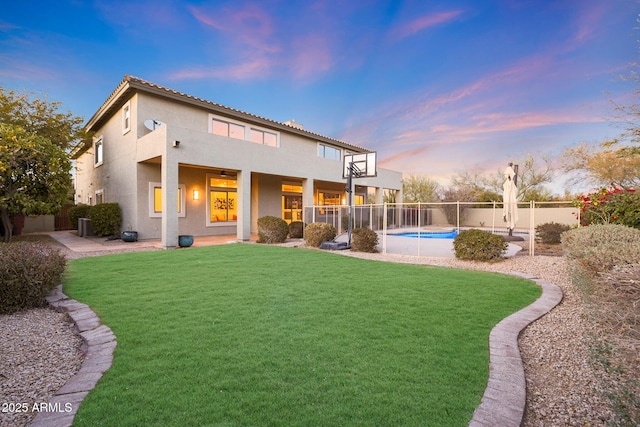 back house at dusk featuring a balcony, a fenced in pool, a patio area, and a yard