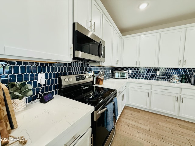 kitchen featuring white cabinets, light wood finished floors, stainless steel appliances, and decorative backsplash