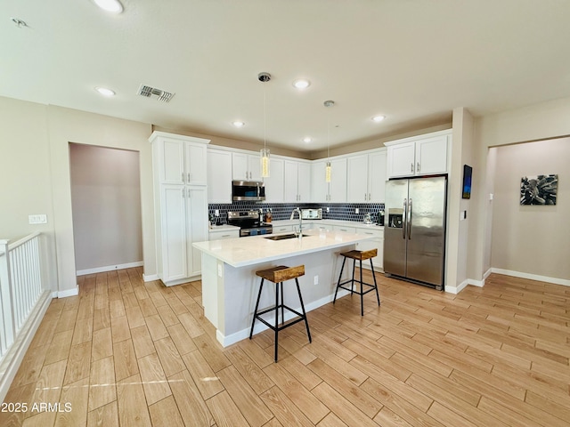 kitchen featuring stainless steel appliances, tasteful backsplash, visible vents, a sink, and light wood-type flooring