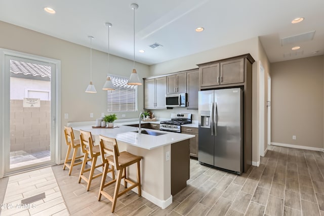 kitchen featuring wood tiled floor, a breakfast bar area, light countertops, stainless steel appliances, and a sink