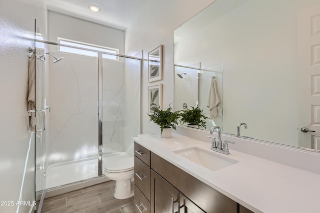 full bathroom with vanity, toilet, a marble finish shower, and wood finish floors