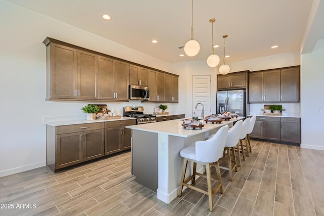 kitchen featuring a kitchen bar, a kitchen island with sink, stainless steel appliances, light countertops, and wood tiled floor