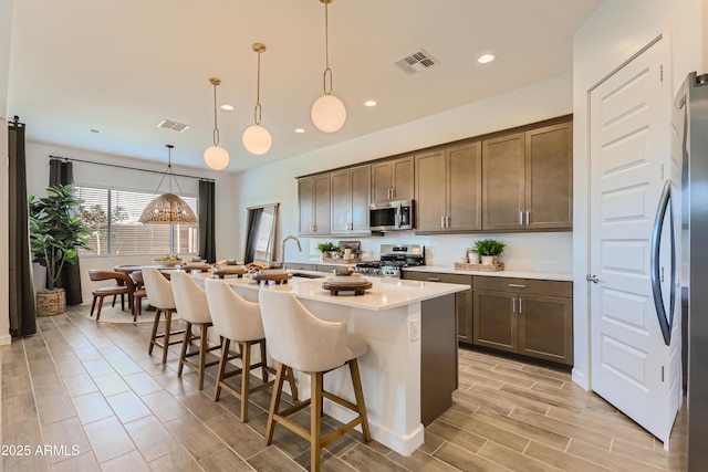 kitchen with visible vents, a center island with sink, light countertops, a kitchen breakfast bar, and stainless steel appliances