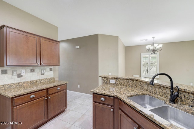 kitchen with light tile patterned flooring, pendant lighting, tasteful backsplash, sink, and light stone counters