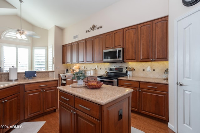 kitchen featuring ceiling fan, appliances with stainless steel finishes, tasteful backsplash, a kitchen island, and vaulted ceiling