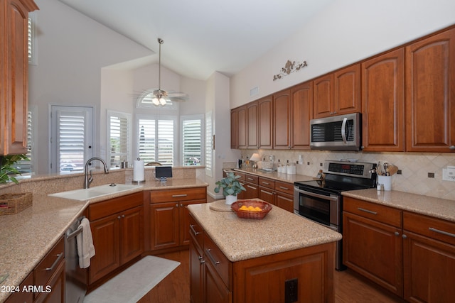 kitchen featuring sink, appliances with stainless steel finishes, a center island, light stone counters, and vaulted ceiling