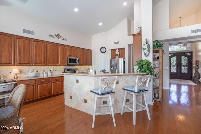 kitchen with high vaulted ceiling, appliances with stainless steel finishes, light hardwood / wood-style floors, and a breakfast bar area