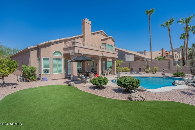 back of property featuring a fenced in pool, a patio area, a balcony, and a lawn