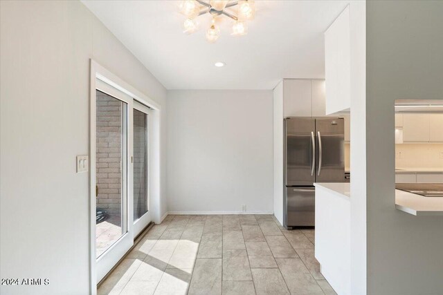 kitchen featuring stainless steel fridge, light tile patterned floors, a chandelier, and white cabinetry